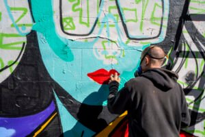 CEPT spray-painting red lips on a turquoise, comic-inspired graffiti mural.