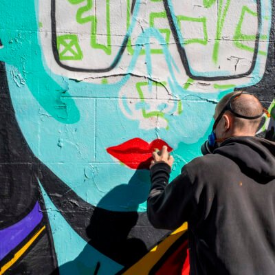 CEPT spray-painting red lips on a turquoise, comic-inspired graffiti mural.